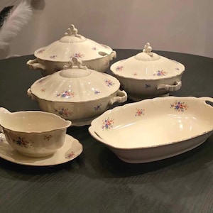 Könnte beinhalten: Ein Set aus vier weißen Porzellangeschirren mit Blumenmustern. Die Gerichte umfassen eine große ovale Servierplatte, zwei runde Servierschalen mit Deckeln und eine kleine Saucierschale mit Untertasse.