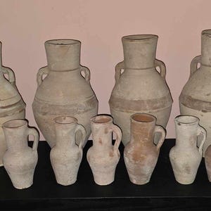 Puede incluir: Una colección de nueve jarras y jarrones de cerámica de diferentes tamaños y formas. Las jarras son todas de color marrón claro y tienen un aspecto rústico y hecho a mano.