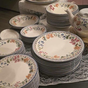 Könnte beinhalten: Ein Set an Keramikgeschirr mit Blumenmuster, bestehend aus Tellern, Schalen und einer Teekanne. Das Geschirr hat einen weißen Hintergrund mit bunten Blumenmustern und blauen Verzierungen.