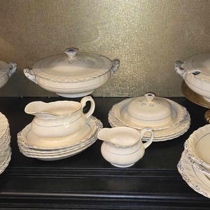 Op de afbeelding: Een set vintage witte porseleinen serveerschalen met blauwe rand. De set bevat een grote serveerschaal, een kleinere serveerschaal, een juskom, een botervloot en verschillende borden.