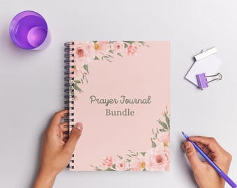 May include: A pink Prayer Journal Bundle with floral accents and the text "Prayer Journal Bundle." The journal is spiral-bound and has a 70-page count. A purple cup, a pen, and a paper clip are also visible.