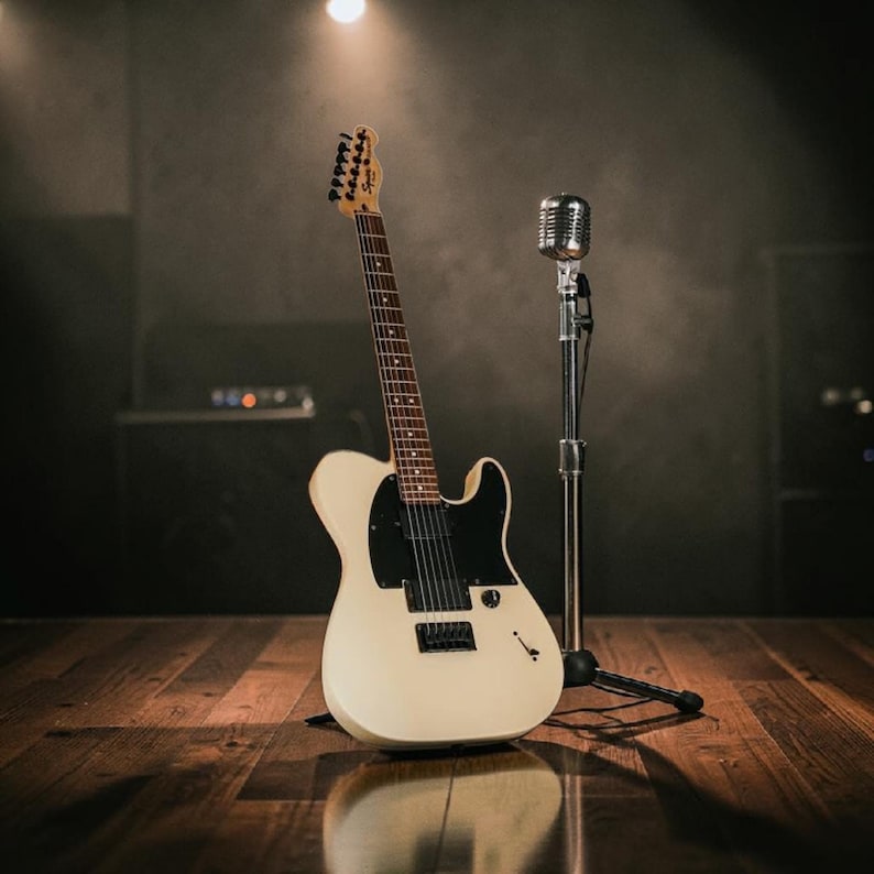 Pu&ograve; includere: Una chitarra elettrica bianco sporco con battipenna nero e un microfono in stile vintage su un supporto. La chitarra &egrave; su un palco di legno, illuminato da un riflettore, che suggerisce un'ambientazione di performance.