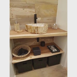 May include: A bathroom vanity with a natural stone sink, black faucet, and wooden countertop. The vanity includes a soap dispenser, a small basket, and storage bins. The wall is tiled with a neutral stone pattern.