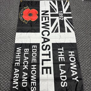 May include: Black and white flag with the text "Newcastle", "Howay The Lads", "Eddie Howes", and "Black and White Army". Features a Union Jack design and a red poppy with the words "Lest We Forget".
