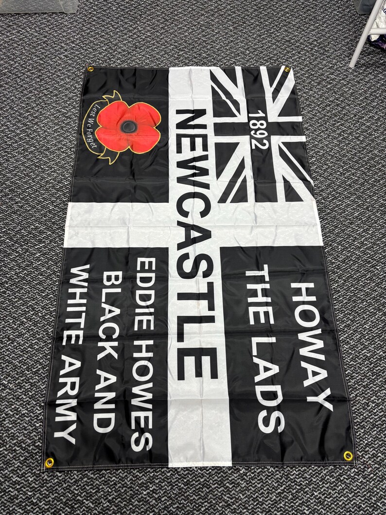 May include: Black and white flag with the text "Newcastle", "Howay The Lads", "Eddie Howes", and "Black and White Army". Features a Union Jack design and a red poppy with the words "Lest We Forget".