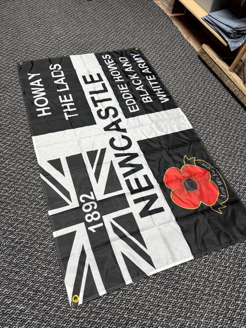 May include: A black and white flag with the text "HOWAY THE LADS" and "NEWCASTLE" in white. The flag features a Union Jack design and a red poppy with the words "Lest We Forget".