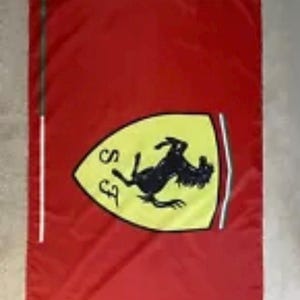 Puede incluir: Una bandera roja con un escudo amarillo que presenta un caballo negro encabritado y las letras "SF" en la esquina superior izquierda.