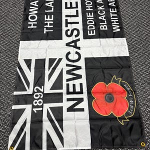 May include: Black and white flag with the text "HOWAY THE LADS" and "NEWCASTLE" in white. Features a Union Jack design and a red poppy with "Lest We Forget" text. Includes the year "1892".