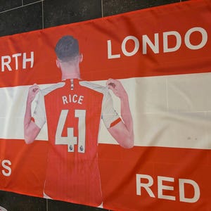 May include: Red and white banner with the text "NORTH LONDON IS RED". The banner features a person wearing a red and white jersey with the name "RICE" and the number "41".