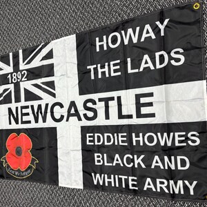 May include: Black and white flag with the text "HOWAY THE LADS NEWCASTLE EDDIE HOWES BLACK AND WHITE ARMY". Features a Union Jack design, the year 1892, and a red poppy with the words "Lest We Forget".