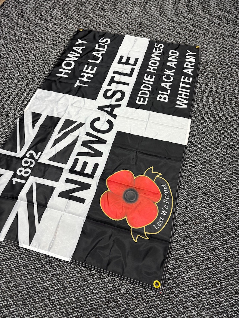 May include: Black and white flag with text that reads "HOWAY THE LADS" and "NEWCASTLE". Features a red poppy with the words "Lest We Forget". Includes the year "1892".