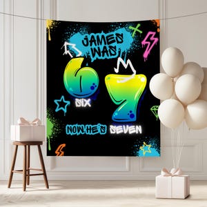 Op de afbeelding: Een zwart verjaardagsbanner met tekst en cijfers in graffitistijl. De banner leest "JAMES WAS 6, NOW HE'S SEVEN" in blauw en wit. De cijfers 6 en 7 hebben een verloop van geel, groen en blauw. Kleurrijke spuitverf accentueert de achtergrond.