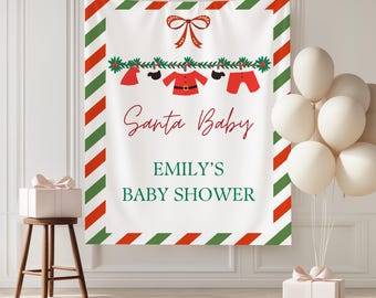 May include: A white banner with red and green striped borders and the text "Santa Baby" in red script. The banner features a clothesline with miniature Santa Claus outfits. The text "EMILY'S BABY SHOWER" is below the main text.