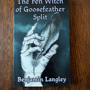 Puede incluir: Portada de libro con fondo azul oscuro y una mano sosteniendo una pluma de ganso blanca. El título es "The Fen Witch of Goosefeather Split" y el autor es "Benjamin Langley".