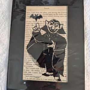 Könnte beinhalten: Eine Schwarzweißillustration von Dracula aus dem Buch "Dracula" von Bram Stoker. Die Illustration zeigt Dracula in einem Umhang mit einer Fledermaus, die über seinem Kopf fliegt. Der Text "Dracula" ist oben im Bild sichtbar.