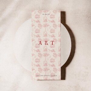 May include: A cream-coloured invitation card with a pink toile pattern of carriages, trees, and buildings. The card displays the initials "A & T" in red, the date "01.06.XX", and the text "The Lake Estate, London".