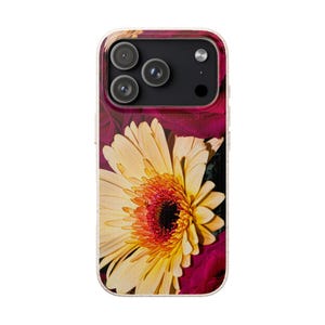 May include: A phone case featuring a close-up of a yellow gerbera daisy with an orange center, set against a background of deep red leaves. The case has a clear, textured border and a black camera module.