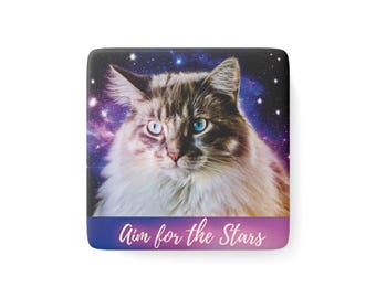 May include: Square product with a cat image, one blue and one light blue eye, set against a starry galaxy backdrop. The bottom has a blue to pink gradient with the text "Aim for the Stars".