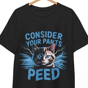 Puede incluir: Camiseta negra con un gráfico de un gato azul y blanco y el texto "Consider Your Pants Peed" en azul.