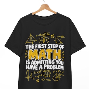 May include: A black short-sleeve t-shirt featuring yellow and white graphic text that reads THE FIRST STEP OF MATH IS ADMITTING YOU HAVE A PROBLEM, surrounded by various mathematical formulas, geometric shapes, and the pi symbol.