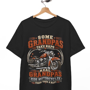 Peut inclure: T-shirt noir avec un motif de moto orange et blanc. Le texte indique "Some Grandpas Take Naps, Real Grandpas Ride Motorcycles (Then Take a Nap)". Le design a un aspect vintage et vieilli.