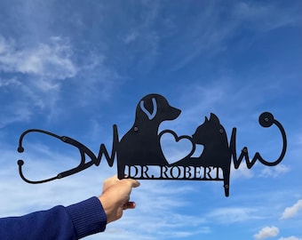 Puede incluir: Silueta de metal negro de un perro y un gato con un estetoscopio y una línea de latido del corazón. El texto "DR. ROBERT" está debajo de los animales.