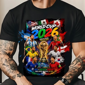 May include: Black t-shirt featuring a colorful graphic for the 2026 World Cup. The design includes the text "World Cup 2026" and images of soccer players, flags, and the FIFA World Cup trophy. The shirt also has the text "United by Passion, Driven by Glory."
