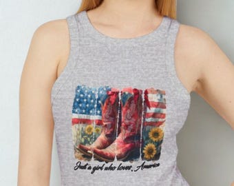May include: Gray tank top featuring a graphic of red cowboy boots, sunflowers, and the American flag. The text "Just a girl who loves America" is printed below the graphic.