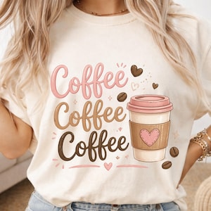 Puede incluir: Una camiseta de color crema con la palabra Coffee impresa tres veces en tonos degradados de rosa, marrón claro y marrón oscuro. A la derecha, un gráfico de una taza de café con tapa rosa y una funda marrón con un corazón rosa.