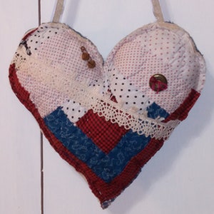 May include: A handmade heart-shaped pillow with a patchwork design in red, white, and blue fabrics. The pillow is decorated with lace and buttons.