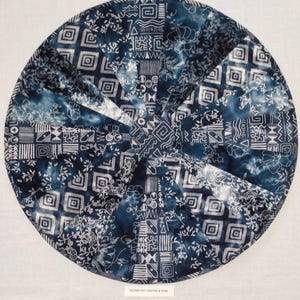 May include: A round blue and white fabric cushion with a geometric pattern. The pattern includes squares, triangles, and wavy lines. The cushion is made of a soft, comfortable fabric.