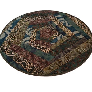 May include: A circular fabric mat featuring a patchwork design of various batik-style patterns in shades of deep teal, forest green, brown, and cream. The textile is constructed from strips arranged in a spiral pattern with a dark brown border.