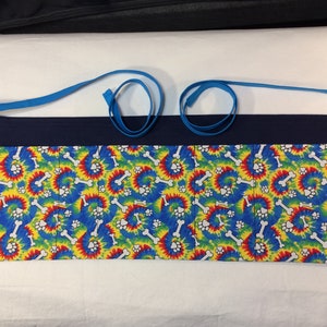 May include: A blue and white tie-dye fabric apron with multiple pockets. The fabric features a pattern of white bones and paw prints on a blue, yellow, red, and green tie-dye background.