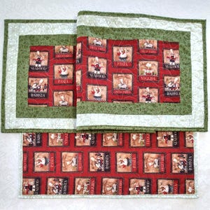 May include: Three quilted placemats with a red background featuring chef illustrations and food-related words. The placemats have a green border with a white inner border.
