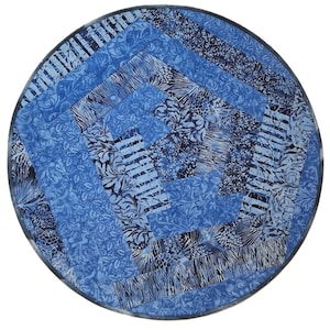 May include: A circular fabric mat featuring a patchwork design of various blue and navy patterned textiles. The quilt-like construction displays alternating strips of floral, botanical, and striped prints arranged in a geometric spiral pattern.