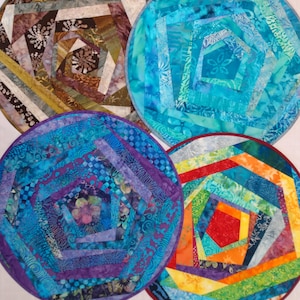 May include: Four colorful, circular quilted placemats. Each placemat features a unique geometric design with a central pentagon shape. The placemats use a variety of fabrics in shades of blue, purple, brown, orange, and green.