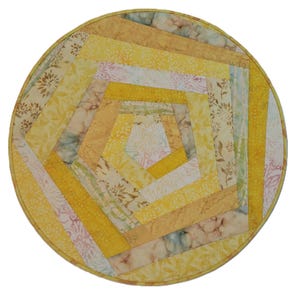 May include: A circular quilted fabric mat featuring a geometric pattern of radiating strips in various shades of yellow, gold, and cream. The design incorporates diverse floral and marbled textures, all enclosed within a matching yellow fabric border.