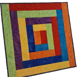 May include: A square quilt featuring a log cabin pattern with concentric rectangular strips in vibrant colors including red, orange, yellow, green, blue, and purple. The fabric displays a subtle textured batik print throughout the entire design.