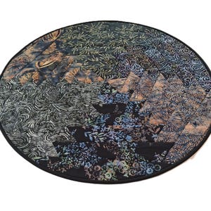 May include: A circular quilted fabric mat featuring a pineapple block pattern. The design is composed of various batik fabrics in shades of black, dark blue, and grey, with intricate floral, swirl, and leaf motifs. It has a solid black fabric border.