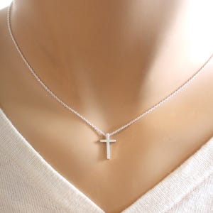 May include: A silver chain necklace with a small silver cross pendant.