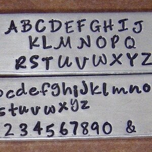 Puede incluir: Una placa de metal con acabado plateado y letras negras. La placa muestra el alfabeto en letras may&uacute;sculas y min&uacute;sculas, as&iacute; como los n&uacute;meros del 1 al 0 y un s&iacute;mbolo de ampersand.