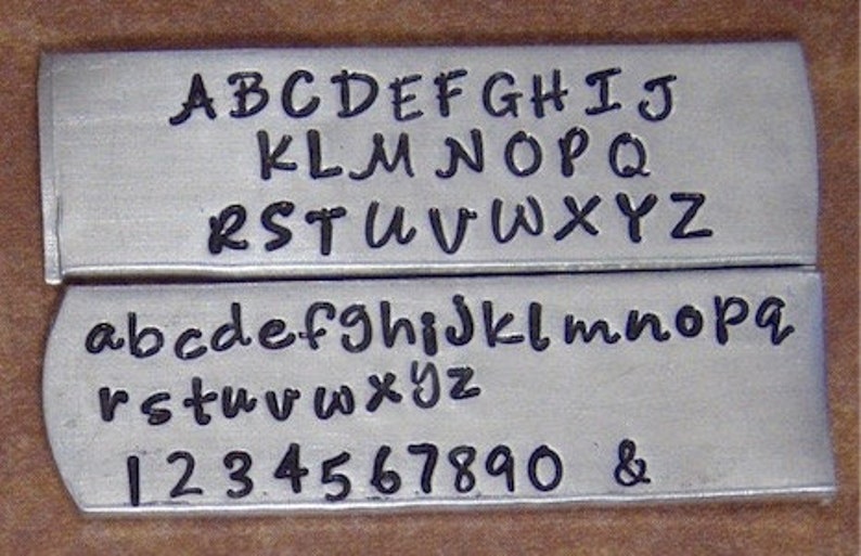 Puede incluir: Una placa de metal con acabado plateado y letras negras. La placa muestra el alfabeto en letras may&uacute;sculas y min&uacute;sculas, as&iacute; como los n&uacute;meros del 1 al 0 y un s&iacute;mbolo de ampersand.