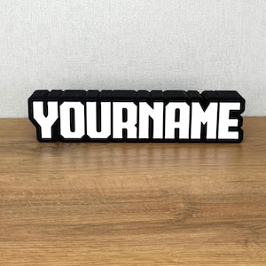 May include: Black block letters spelling out "YOURNAME" in white letters. The letters are raised and have a 3D effect.