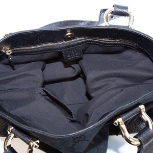 May include: Black tote bag with gold-tone hardware. The interior is black with a zippered pocket. The bag has two handles and a magnetic snap closure. The exterior features a subtle pattern.