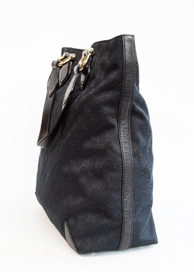 May include: Black tote bag with a repeating pattern of interlocking Gs. The bag features leather trim, gold-tone hardware, and a shoulder strap. The bag is made of a durable fabric.