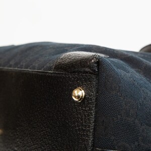 May include: Close-up of a black handbag with a navy blue fabric body. The bag features black leather trim and gold-colored metal studs. The navy blue fabric has a repeating pattern.