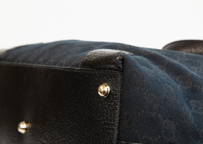 May include: Close-up of a black handbag with a navy blue fabric body. The bag features black leather trim and gold-colored metal studs. The navy blue fabric has a repeating pattern.