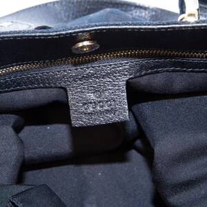 May include: Close-up of a black leather handbag with a gold zipper and hardware. The interior is lined with black fabric. A leather tag with the "GUCCI" logo is visible.