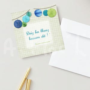 May include: A square greeting card with a grid pattern, adorned with blue, green, and turquoise paper decorations. The card features the text "Deiz ha bloaz laouen dit !" and "Joyeux anniversaire !" in a teal font, with a white envelope.
