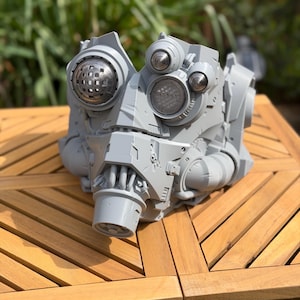 May include: A light grey, 3D-printed sci-fi helmet featuring a complex mechanical design with multiple circular lens-like eye pieces, a prominent central breathing apparatus, and various angular panels and tubing details across the exterior surface.